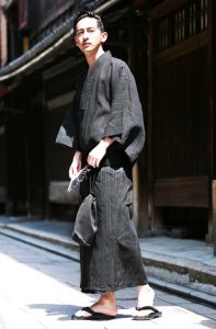 A Man in Charcoal Gray Yukata holding a fan and a purse